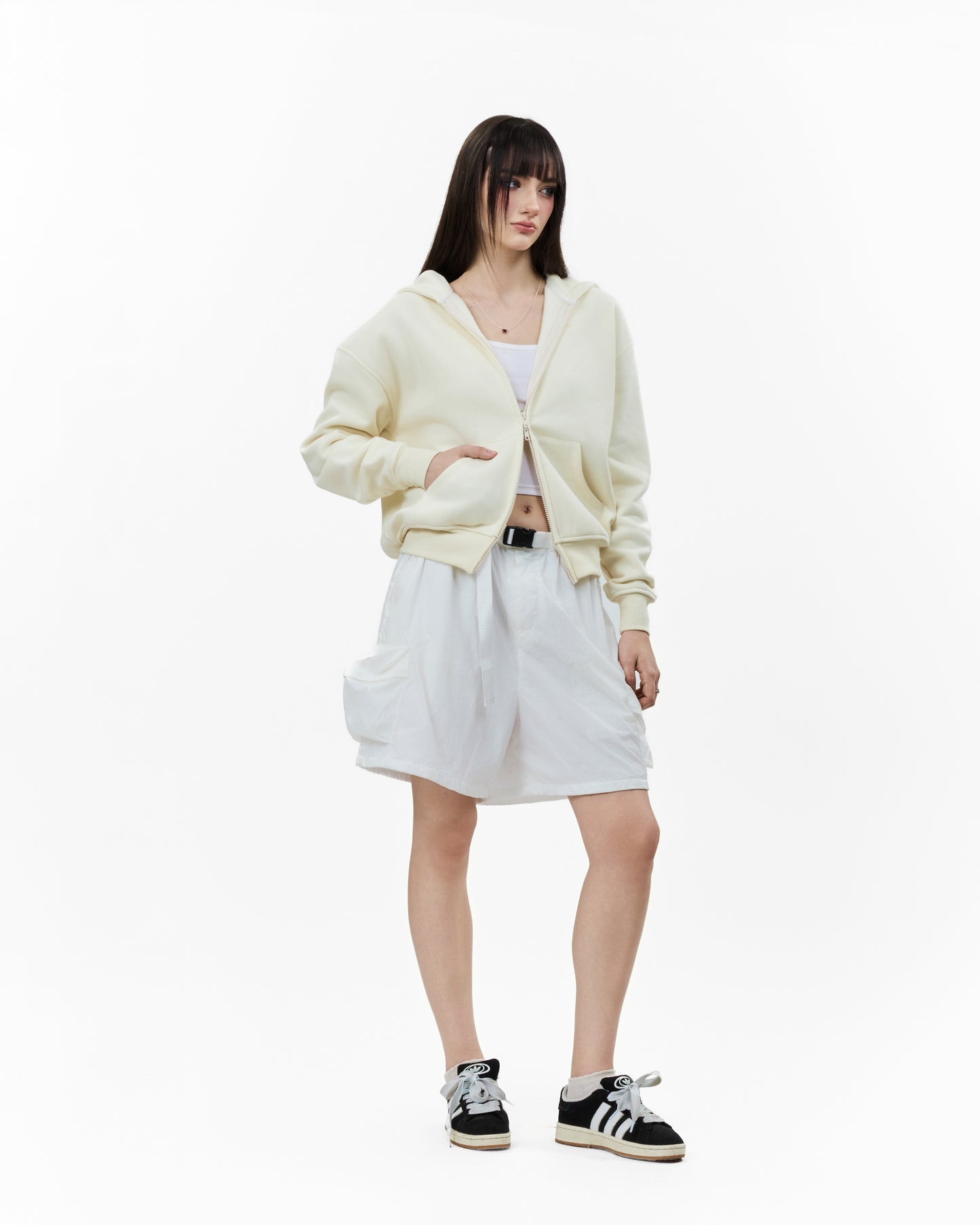 Young woman wearing the LAVIEM Boxy Double-Zip Hoodie in beige layered over a white tank top, showcasing the cropped streetwear fit and dual zippers for a casual urban look.