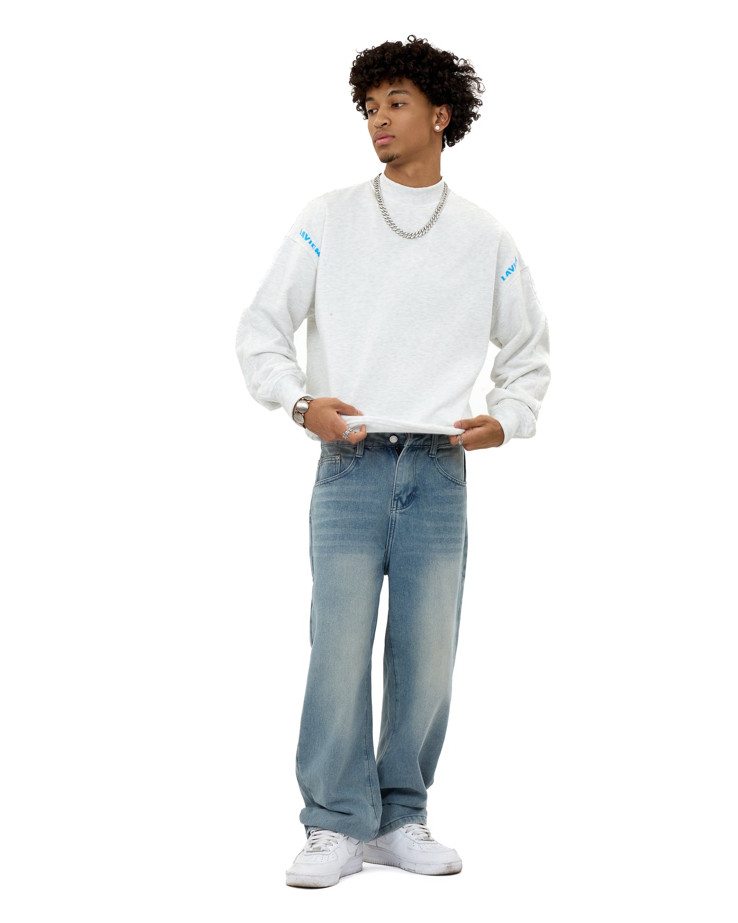 Male model wearing the LAVIEM Oversized Sweater in grey – a cotton streetwear sweatshirt with a relaxed fit – styled with light-wash baggy jeans, white sneakers, silver chain necklace and stud earrings for casual urban menswear.