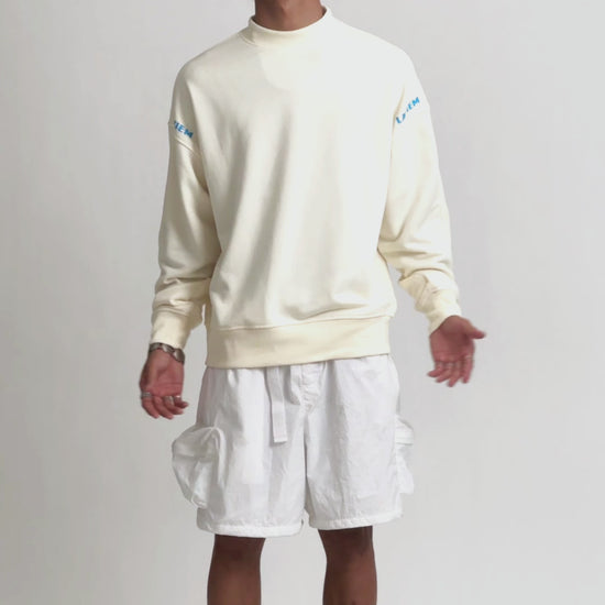 Video of a male model showcasing the LAVIEM Oversized Sweater, a 100% cotton streetwear sweatshirt with a relaxed, boxy fit. It highlightes the sweater’s drape and comfort, styled with baggy jeans, cargo shorts and white sneakers for an urban menswear look.